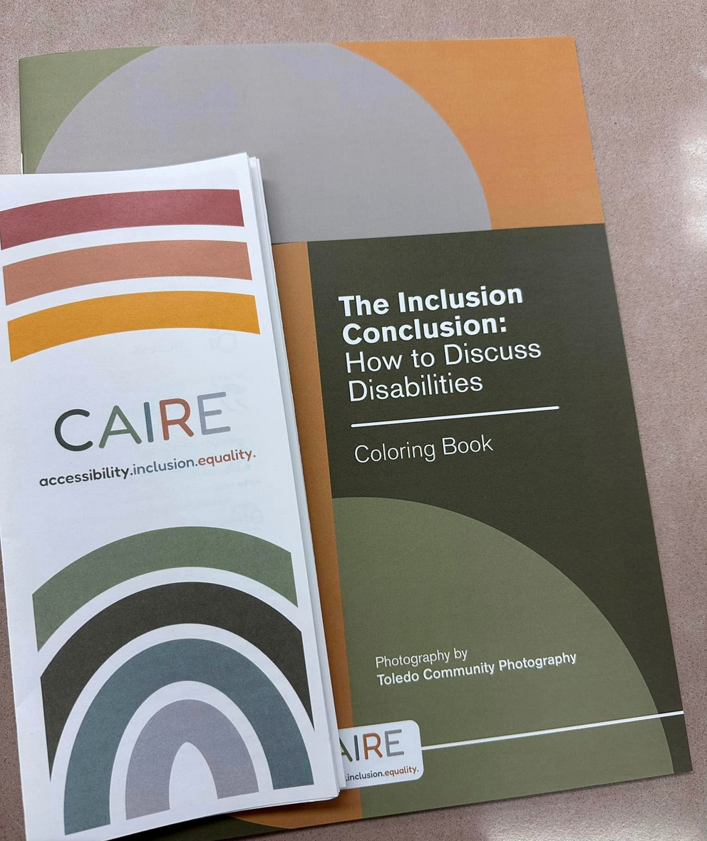 A copy of a CAIRE LLC pamphlet sits on top of the coloring book, "The Inclusion Conclusion."