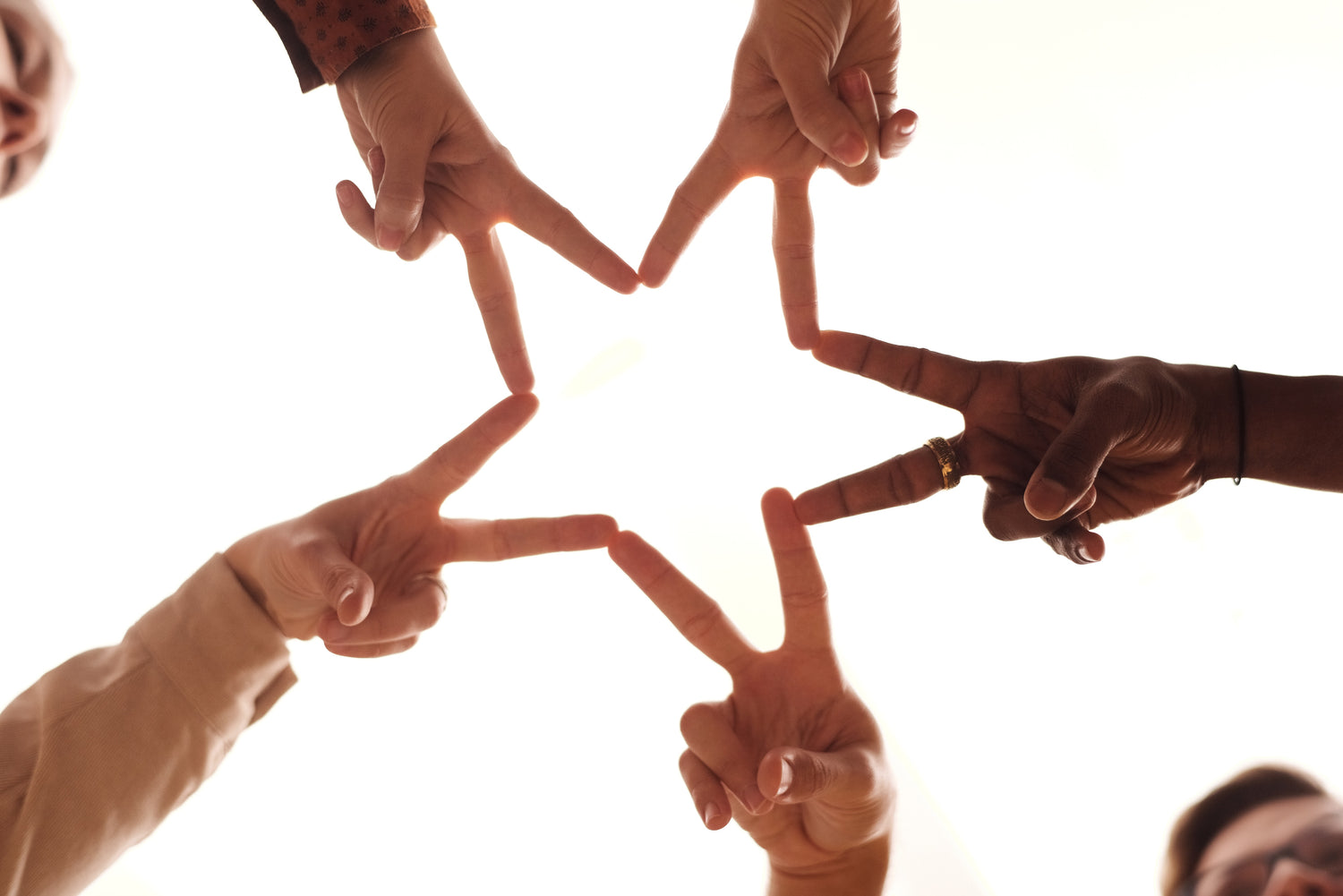 Five hands with varying skin tones put tow fingers out in a V shape to create a star shape together. 